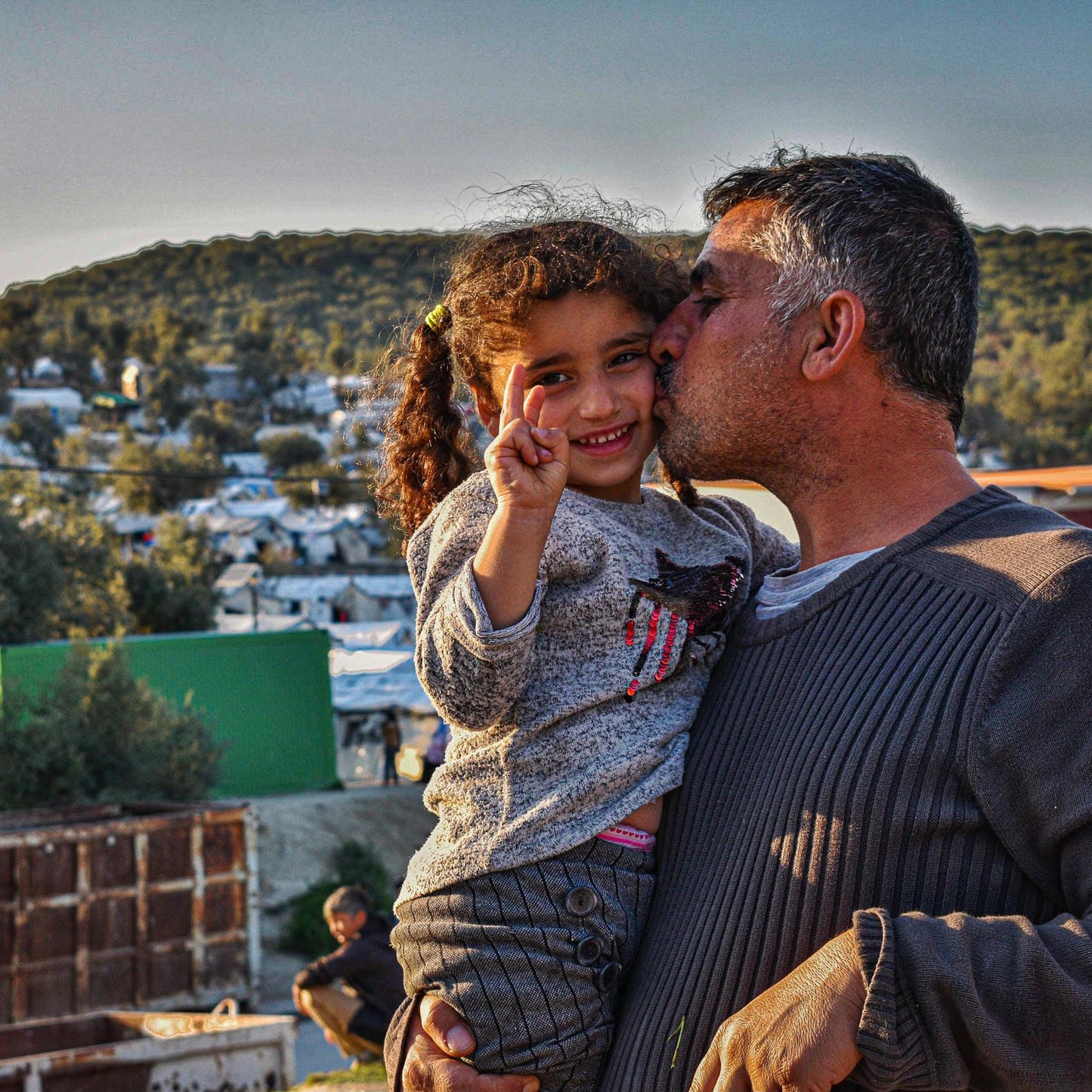 Father holds child in front of camp
