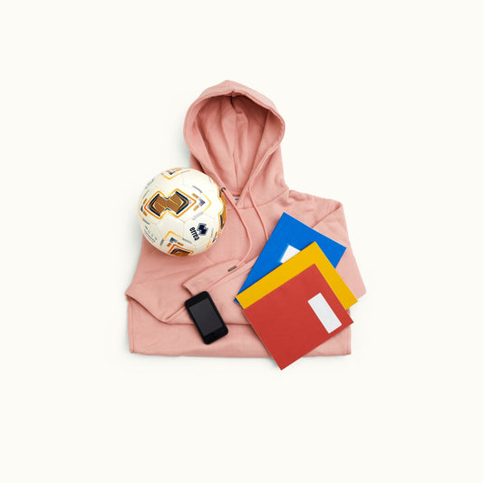 This image shows a hoodie layed flat with a football placed on it, a mobile phone and 3 notebooks.